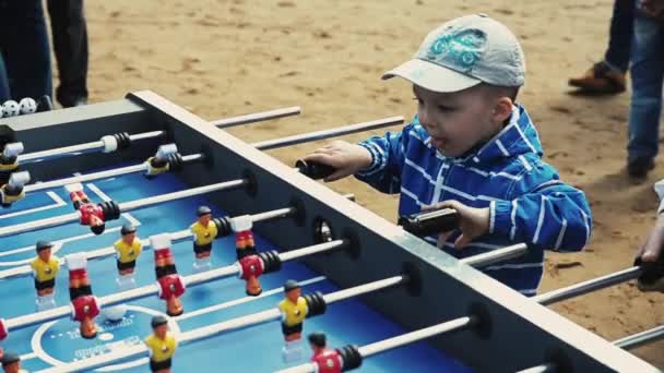 SAINT PETERSBURG, RUSSIA - SEPTEMBER 6, 2014: Little boy in cap absorbedly play american table soccer with adult. Sand. People — Αρχείο Βίντεο
