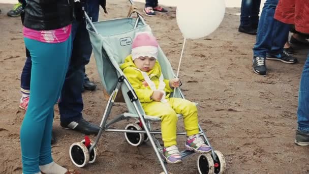 СЕНТ-ПЕТЕРБУРГ, РОССИЯ - 6 СЕНТЯБРЯ 2014 г.: Маленькая девочка в жёлтом костюме держит воздушный шарик в коляске. Летний фестиваль. Люди — стоковое видео