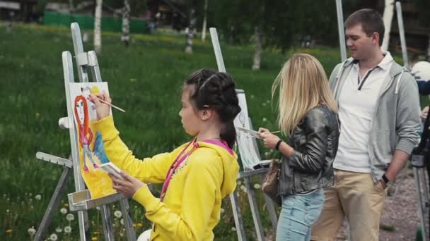 SAINT PETERSBURG, RUSIA - SEPTEMBRIE 6, 2014: Fata desenează pictura pe șevalet în parcul verde la festivalul de vară, printre alte persoane — Videoclip de stoc