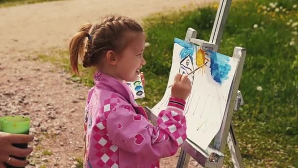 Saint Petersburg, Federacja Rosyjska - 6 września 2014: Mała dziewczynka rysuje obraz na sztalugach w parku na letni festiwal. Uśmiech w aparacie — Wideo stockowe
