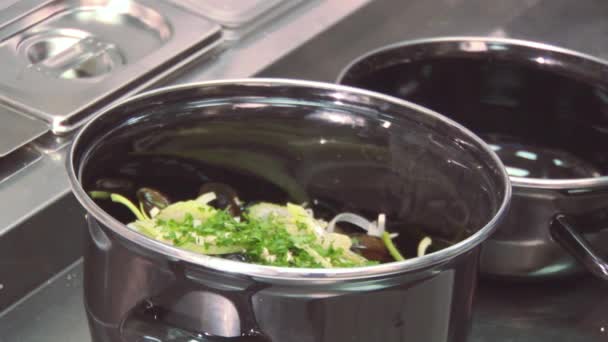 Cook add basil from plastic container in pan with mussels, greenery on table. Restaurant kitchen — Stock Video