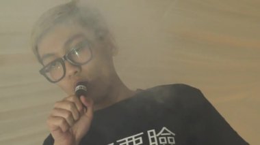 Gözlüklü Asyalı genç çocuk nefes elektronik sigara çift yüzük. Vaper.