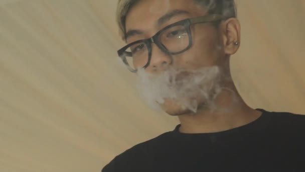 Menino asiático em óculos exalar vapor de cigarro eletrônico. O Vaper. Tabagista . — Vídeo de Stock