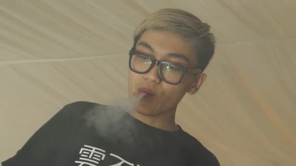 Asiatisk pojke i glas göra cirklar från elektronisk cigarett steam. Vaper — Stockvideo