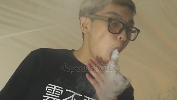 Asiatischer kleiner Junge in Brille atmet Ringe aus der elektronischen Zigarette aus. Dampf ab. Raucher — Stockvideo