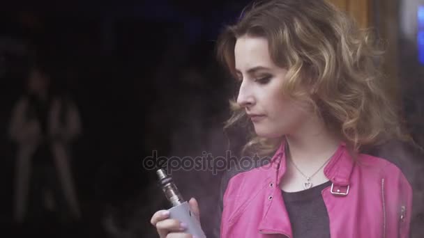 Girl in pink jacket exhalation smoke from electronic cigarette on street. Vaper — Stock Video