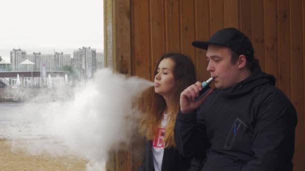女孩和男人呼气蒸汽从街上的电子香烟。云顶。吸烟者 — 图库视频影像