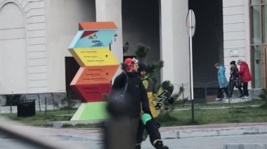 Sochi, Rusya - 27 Mart 2016: Üniformalı iki snowboard düşkünleri görünümünü, kask sokak, binalar üzerinde yürümek. Şehirde akşam. Yeşil ağaçlar