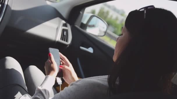 Młoda brunetka dziewczyna siedzi w środku jazda samochodem na fotelu pasażera. Stuknij pozycję telefon. Słoneczny dzień lata — Wideo stockowe