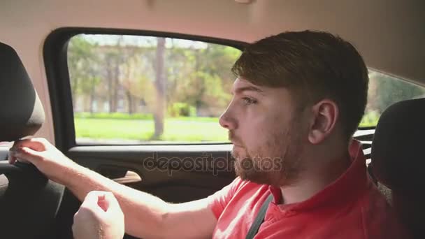 Joven barbudo sentado en el interior del coche en el asiento trasero. Tocando el pelo. Día soleado de verano — Vídeos de Stock
