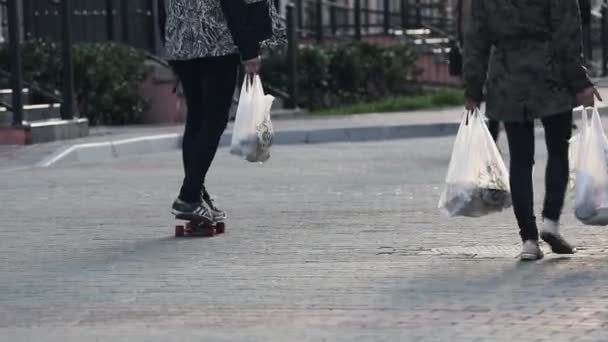 Sochi, Ryssland - den 27 mars 2016: Tillbaka sida av tre vänner promenad på gatan med stora vita paket. En man på skateboard. Kvällen — Stockvideo