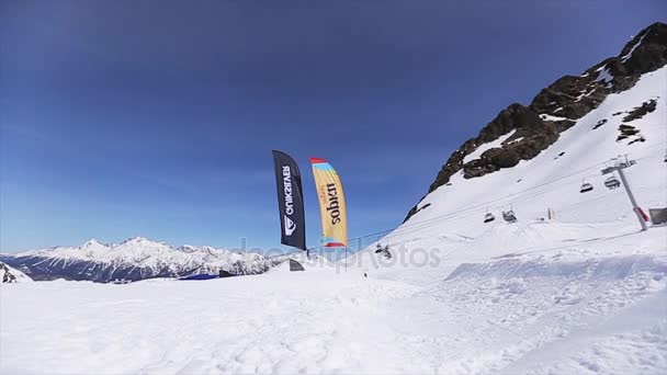 SOCHI, RUSIA - 1 DE ABRIL DE 2016: Salto de snowboard desde trampolín en cámara frontal. Montañas de paisaje. Cielo azul — Vídeo de stock