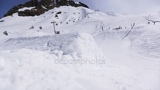 СОЧИ, РОССИЯ - 1 апреля 2016 года: прыжок сноубордиста с трамплина перед камерой. Вид на горы. Голубое небо — стоковое видео