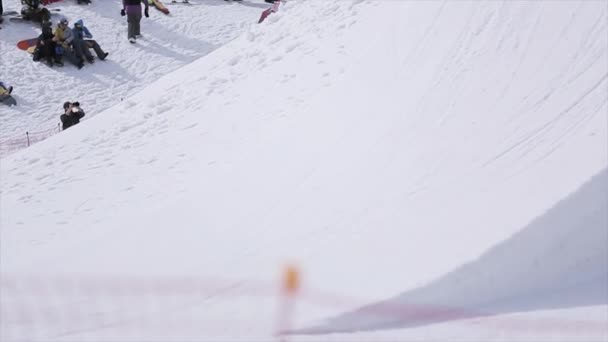SOCHI, RUSIA - 1 DE ABRIL DE 2016: Salto snowboarder desde trampolín hacer volteretas, flexiona los pies. La gente se relaja en la pendiente — Vídeo de stock