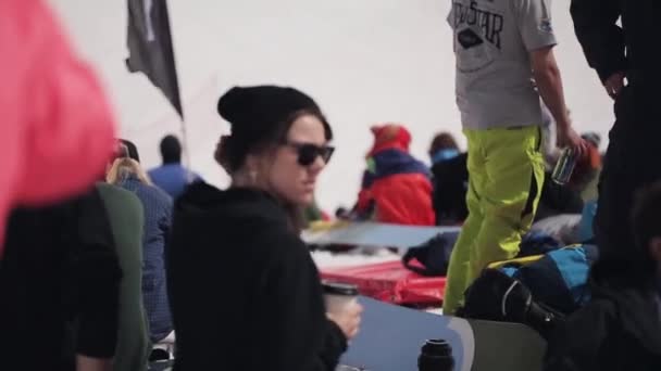 SOCHI, RUSIA - 1 DE ABRIL DE 2016: La gente se relaja en el campamento. Estación de esquí. Chica con sombrero, gafas de sol beber café. Soleado. — Vídeos de Stock