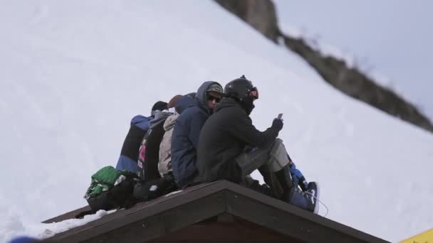 Sochi, Російська Федерація - 1 квітня 2016: Гірськолижний курорт. Енкамп сноубордисти, сидячи на даху будинку в. Натовп людей — стокове відео