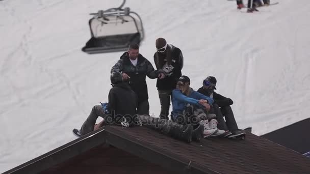 SOCHI, RUSSIA - 1 APRILE 2016: Comprensorio sciistico. Snowboarder seduti sul tetto della casa nell'accampamento. Giro sugli impianti di risalita . — Video Stock