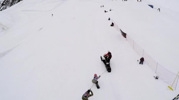 SOCHI, RUSSIA - APRIL 4, 2016: Quadrocopter shoot snowboarders hold on rope driving snowmobile on slope — Stok Video