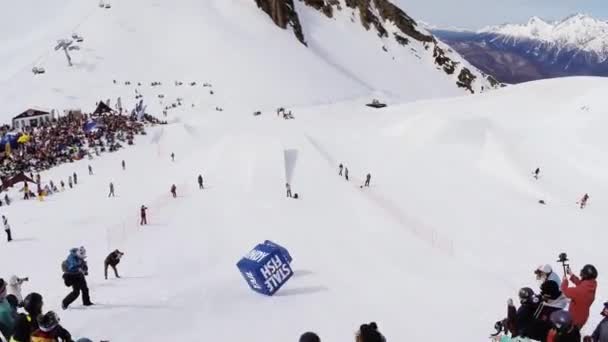 Sochi, Rusko - duben 4, 2016: Quadrocopter natáčení snowboardisté zůstat na odrazový můstek, hoď modré kostky na svahu — Stock video
