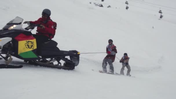 SOCHI, RÚSSIA - 4 de abril de 2016: snowboarders passeio em snowmobile segurar na corda. Estância de esqui. Entretenimento extremo — Vídeo de Stock