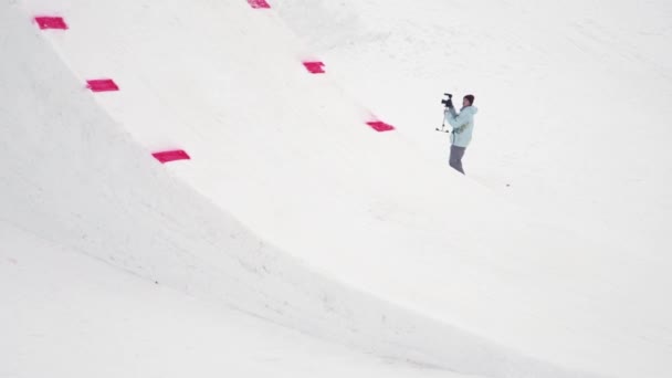 Sochi, Rusko - duben 4, 2016: Snowboardista jízdu na odrazový můstek, aby překlopit ve vzduchu. Zasněžené hory. Kameraman. — Stock video