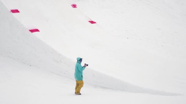 Sochi, Rusko - duben 4, 2016: Kameraman střílet snowboardista jízdu na odrazový můstek, překlopit ve vzduchu. Zasněžené hory. — Stock video