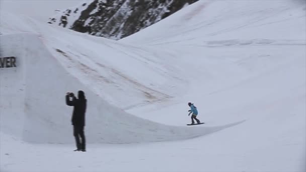 Sochi, Ryssland - April 4, 2016: Snowboardåkare höjdhopp från springboard. Skidorten. Grått väder. Kameramannen. — Stockvideo