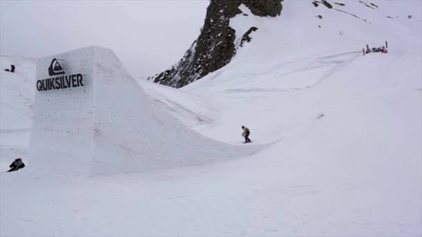 Sochi, Rusland - 4 April 2016: Snowboarder sprong van hoge springplank, maken spiegelen. Rode blokjes. Bergen. — Stockvideo