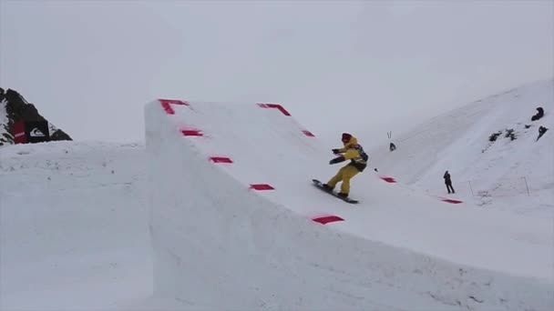 SOCHI, RUSIA - 4 DE ABRIL DE 2016: Snowboarder en traje amarillo salta desde un trampolín alto, hace un giro extremo en el aire . — Vídeos de Stock