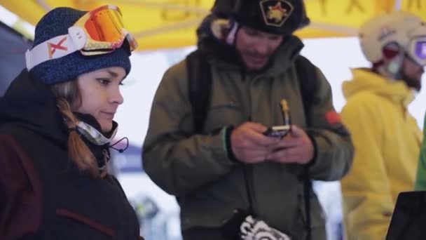 Sochi, Ryssland - April 4, 2016: Snowboardåkare och skidåkare i encamp på skidorten. Mannen i öronlappar använda smartphone — Stockvideo