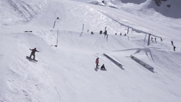 Sochi, Ryssland - April 1, 2016: Ski resort. Snowboardåkare rida från backen. Språngbrädor. Vita bergen. Soligt — Stockvideo