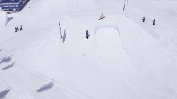 Sochi, Rusko - 1. dubna 2016: Lyžařské středisko. Snowboardista skok do výšky z odrazový můstek. Překlopte. Zasněžené hory. Slunečno — Stock video