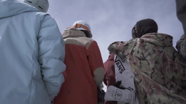 SOCHI, RÚSSIA - 1 de abril de 2016: A parte de trás dos snowboarders e esquiadores fica no topo da encosta. Capacete. Dia ensolarado . — Vídeo de Stock