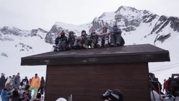 Sochi, Російська Федерація - 1 квітня 2016: Гірськолижний курорт. Енкамп сноубордисти, сидячи на даху будинку в. Помахом руки в камери — стокове відео