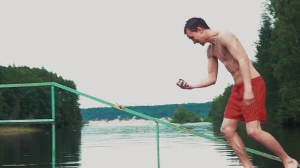 Young man running to water at lake with go pro camera in hands. Summer. Emotions — Stock Video