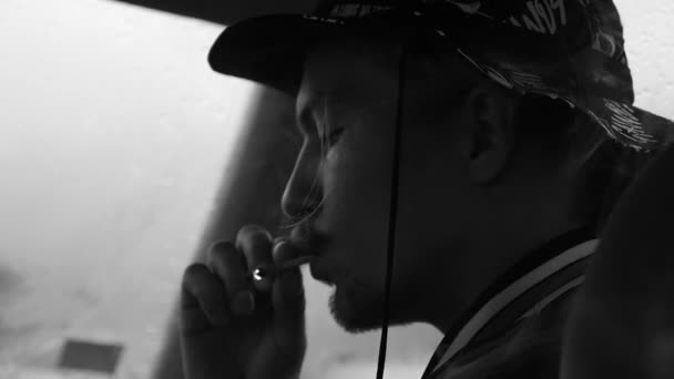 Un joven fuma cigarrillos en el auto. Blanco y negro. Exhala y respira humo . — Vídeos de Stock