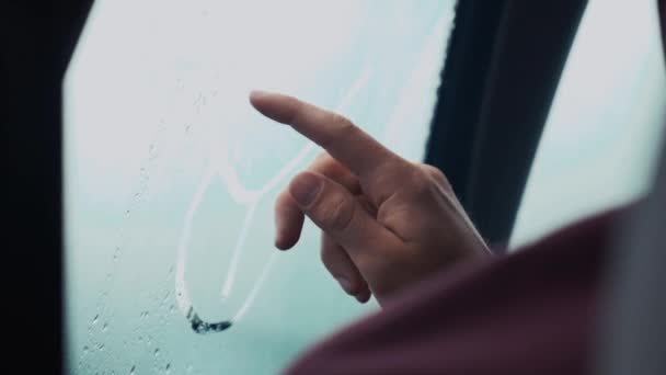 Hombre dibujando en la ventana interior del coche por un dedo. Clima lluvioso afuera. Gotas — Vídeo de stock