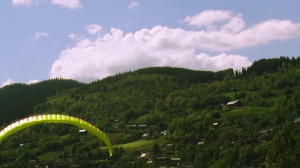 Panoráma a hegyek borított zöld erdőben a nyári napsütésben. Kék ég. Sárga ejtőernyős — Stock videók