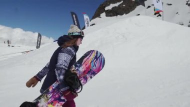 Sochi, Rusya Federasyonu - 7 Nisan 2016: Kız ile snowboard Kayak Merkezi üzerinde yürümek. Kamera dilini göster. Gülümse. Güneşli