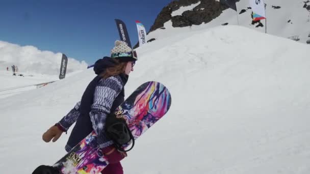 Sochi, Російська Федерація - 7 квітня 2016: Дівчина з сноуборд прогулянка на гірськолижному курорті. Показати язика в камеру. Посмішка. Сонячно — стокове відео