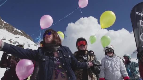 SOCHI, RUSIA - 7 DE ABRIL DE 2016: Chica con gafas de sol reparte globos aéreos a las personas en la estación de esquí. Entretenimiento . — Vídeo de stock