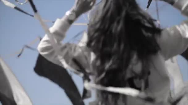 Ein fröhliches Mädchen in Kapuzenpulli und Sonnenbrille hebt die Hände zwischen schwenkenden Bändern. windiger Tag. schwarz-weiß — Stockvideo