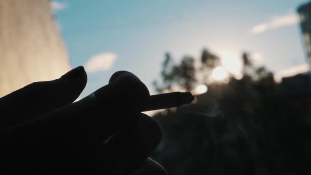 Lento primer plano silueta de la mano sosteniendo el cigarrillo afuera en sol brillante — Vídeo de stock