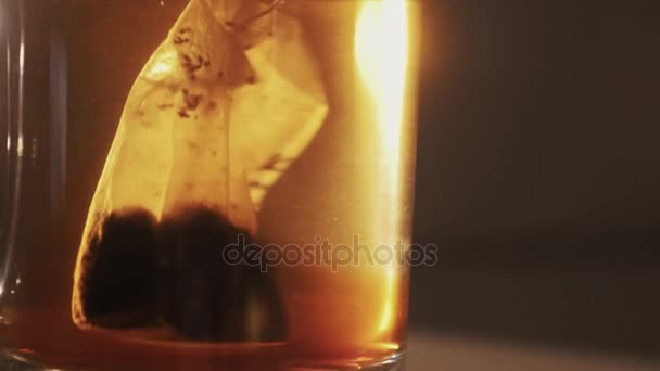 Slowmotion close up tea bag pulled up and down in transparent glass of water — Stock Video