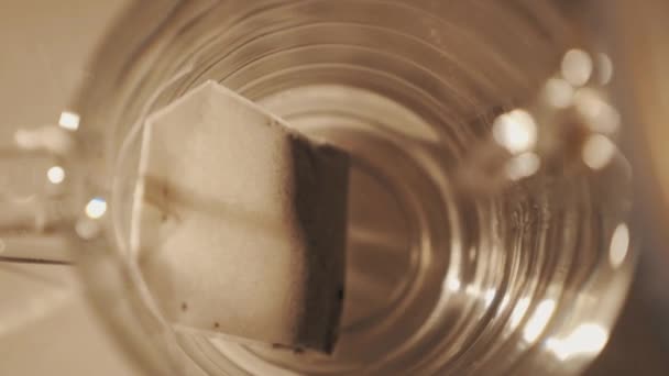 Close-up van tikje water gieten in transparent glazen beker met theezakje in het — Stockvideo