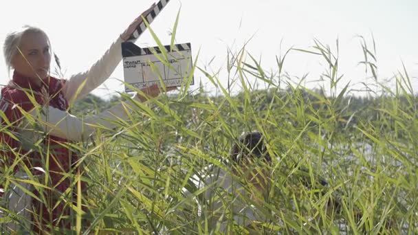 Клаппер перед кинорежиссером в сетке для волос выделяется тростником и гримасой — стоковое видео