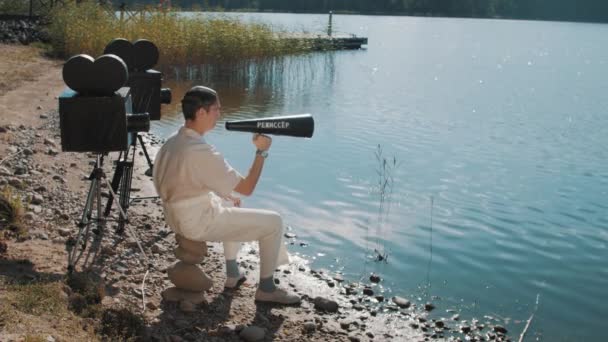 Filmregisseur in Haarnetz frisst mit zwei Kameras Trauben aus Lautsprecher am Seeufer — Stockvideo