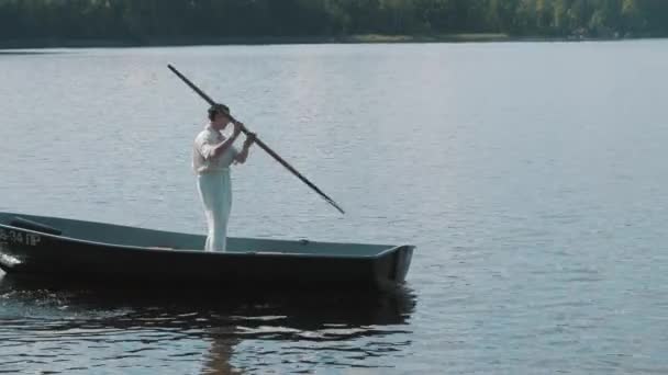 Homme en filet à cheveux et vêtements blancs debout sur le bateau pagaie sur le lac — Video