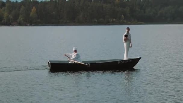 Zdravotní sestra pádlování loď na jezeře, muž v bílých šatech příkazy do megafon — Stock video
