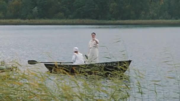 Nurse paddling boat on lake, man in hair net yelling into megaphone — Stock Video